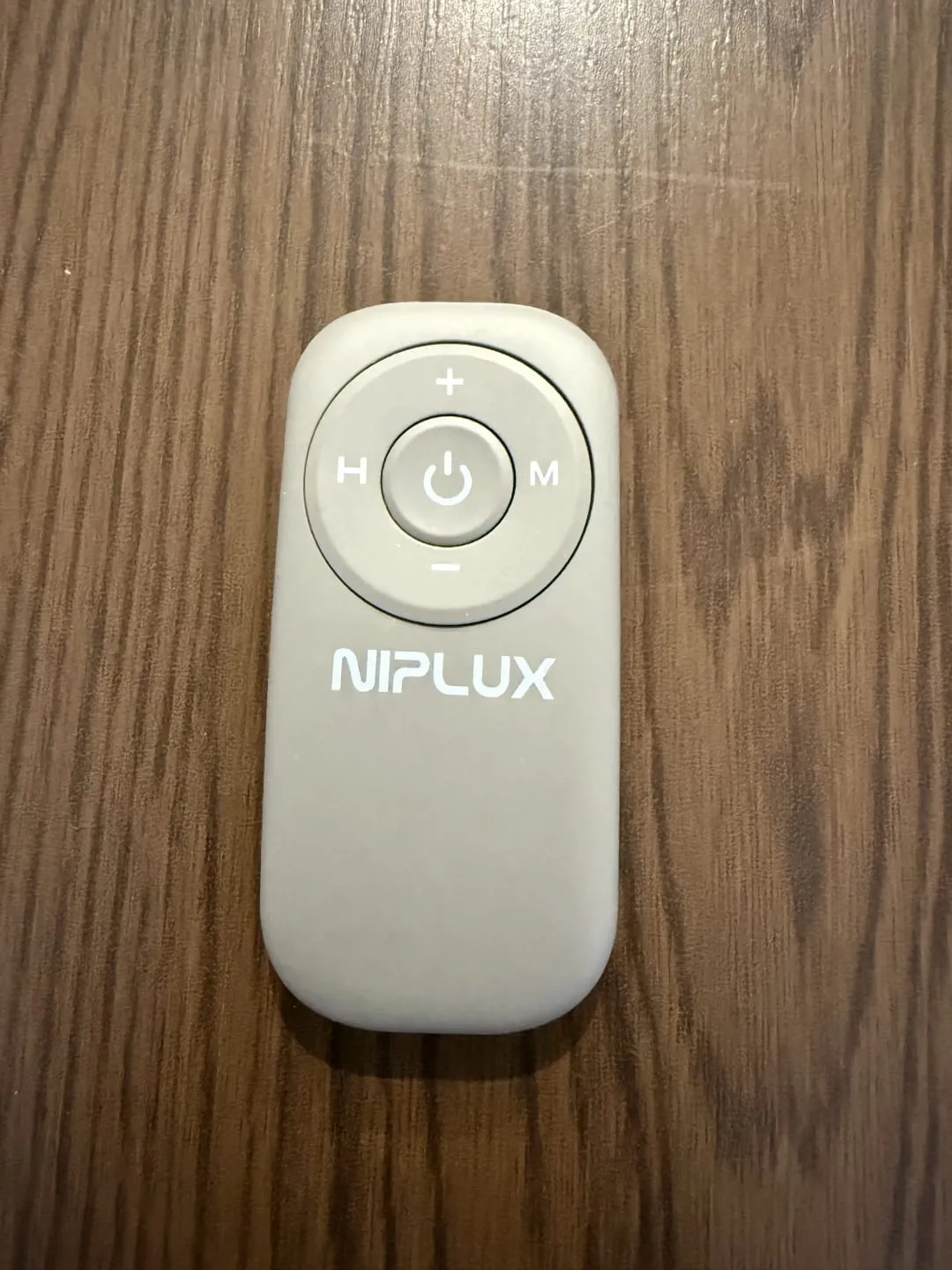 NIPLUX NECK PREMSのリモコン。中央に電源、上下に強弱(+/-)、左にH(温熱)、右にM(モード)ボタン
